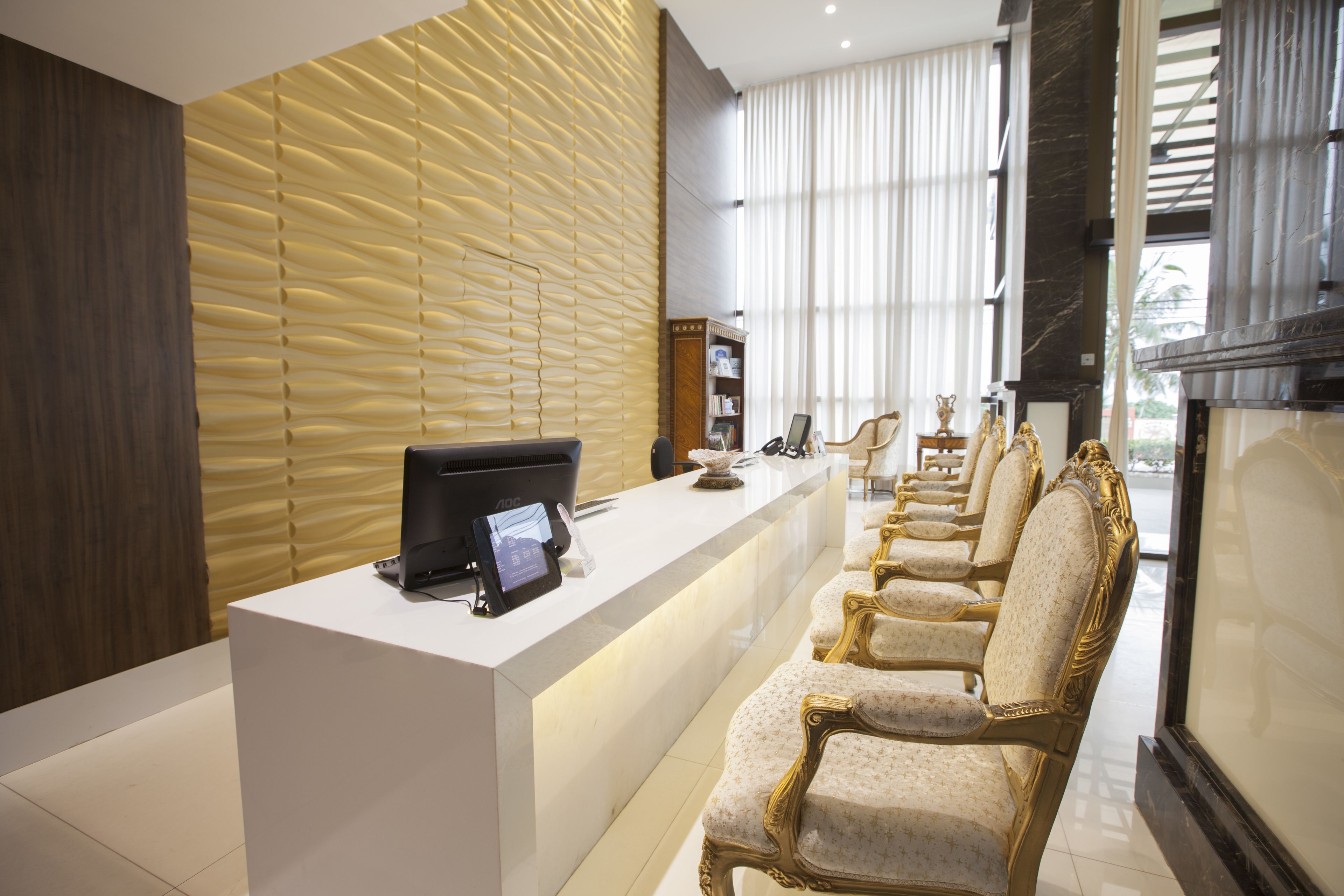 A reception area with a modern desk, a seating area with ornate chairs, a bookshelf, and a large window with curtains.