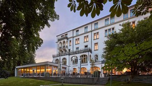 A multi-story hotel with a glass facade, outdoor seating area, and a stone staircase leading to the entrance. - Dorint Parkhotel Jordanbad Biberach an der Riß (Biberach an der Riss)