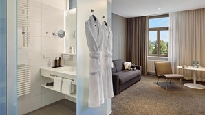 A modern hotel room with a large mirror, white towels, a sofa, a chair, and a small table with toiletries. - Dorint Parkhotel Jordanbad Biberach an der Riß (Biberach an der Riss)