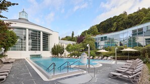 A modern pool area with lounge chairs, a glass building, and a stone pathway. - Dorint Parkhotel Jordanbad Biberach an der Riß (Biberach an der Riss)