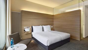 Una habitación de hotel moderna con una cama grande, una zona de estar con una mesa y un armario.