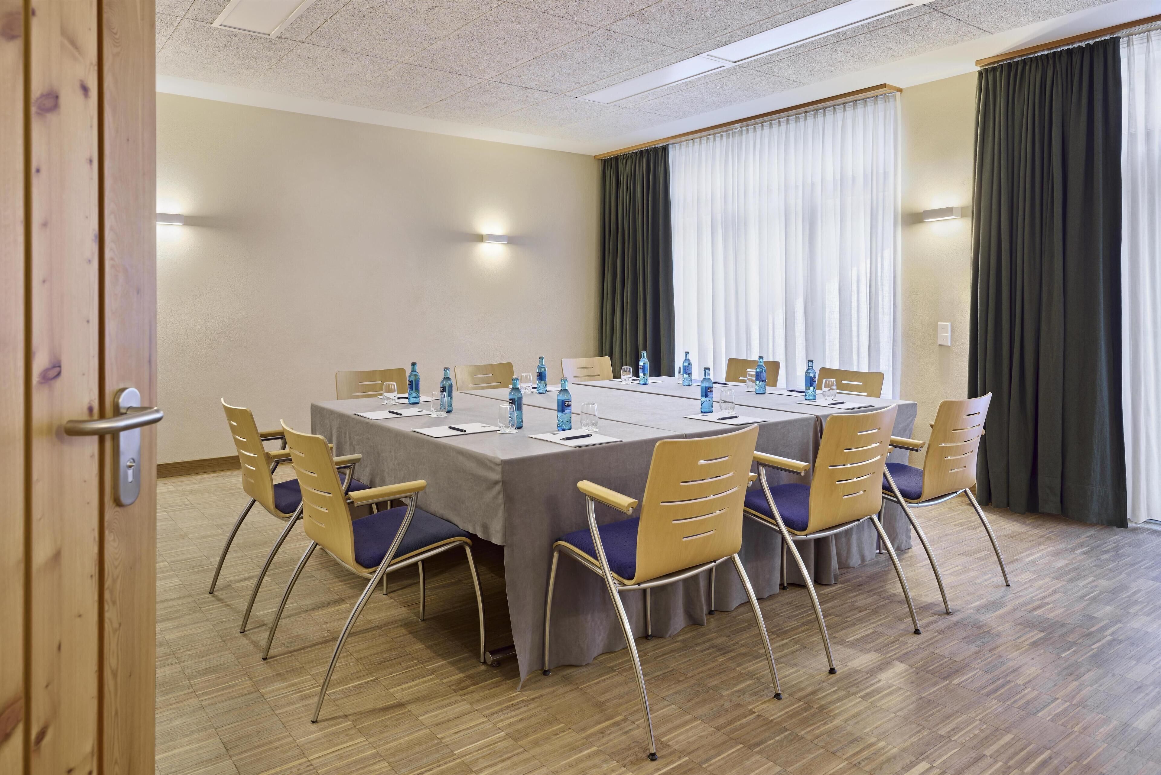 Un salón de conferencias con una larga mesa, sillas y botellas de agua.