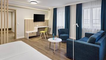 Une chambre d’hôtel moderne dotée d’un grand lit, d’un bureau avec une chaise, d’un canapé, d’un téléviseur fixé au mur et d’une fenêtre avec des rideaux.
