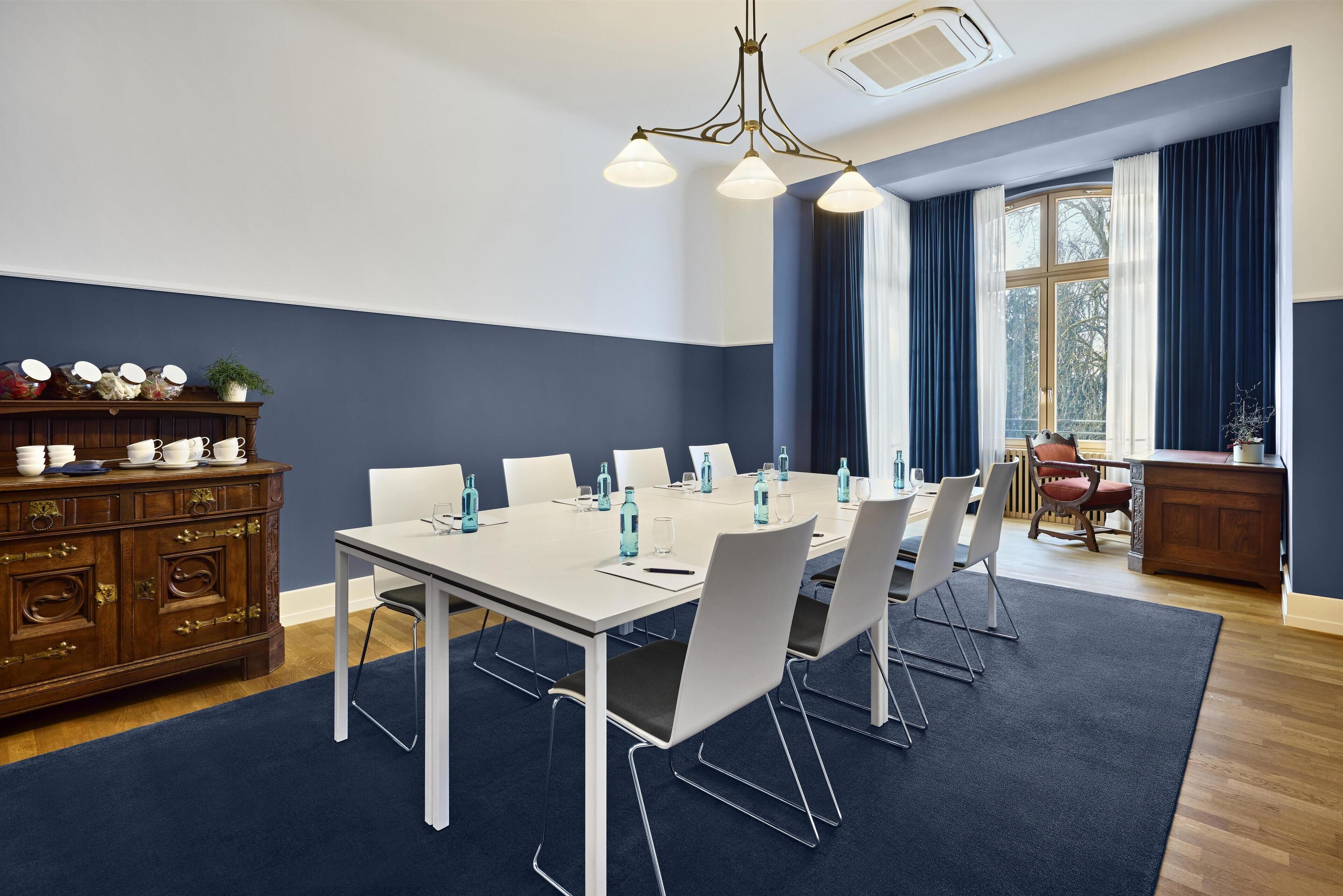 A conference room with a white table, chairs, and a wooden cabinet with dishes.