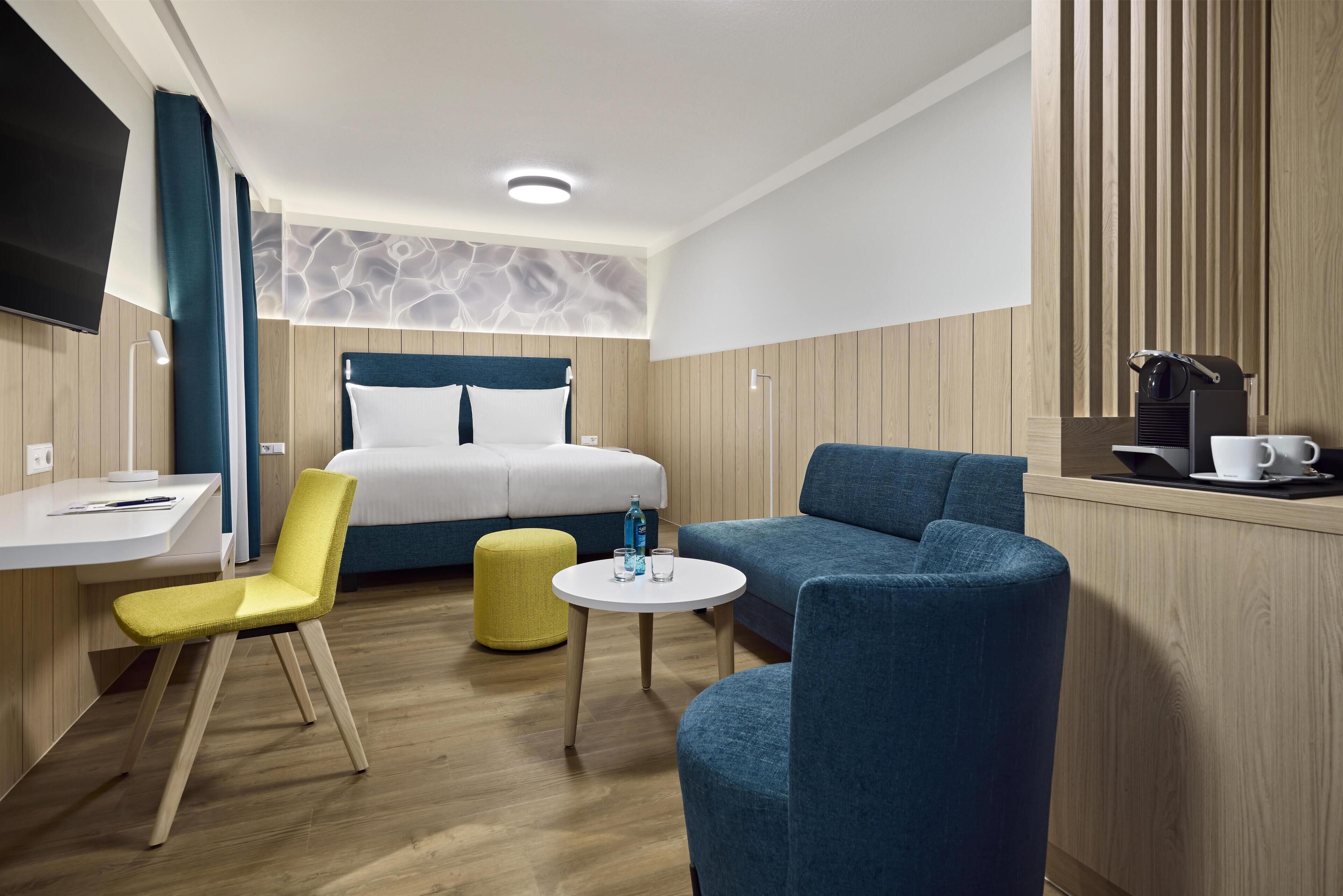 Een moderne hotelkamer met een bed, een bureau, een stoel, een bank en een klein rond tafeltje.