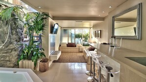 A modern kitchen with a bar area, a large mirror, and a view of the living area. - Clifton Bungalow (Cape Town)