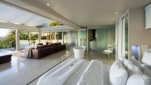A modern bedroom with a large bed, a sitting area with a sofa and a coffee table, a bathtub, and a view of the ocean. - Clifton Bungalow (Cape Town)