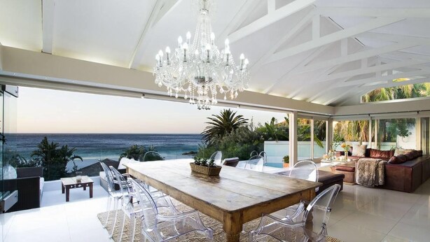 A spacious living area with a large wooden table and chairs, a chandelier, and a view of the ocean. - Clifton Bungalow (Cape Town)