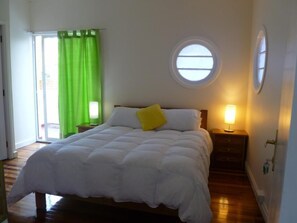 Ein Schlafzimmer mit Bett, Fenster, Nachttisch und einem grünen Vorhang.