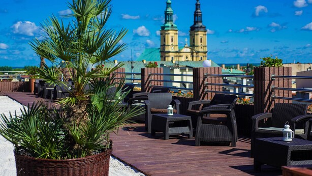 A rooftop terrace with wicker furniture, a potted plant, and a view of a historic building with two spires.