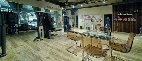 A modern fitness center with exercise equipment, a glass table, and chairs.