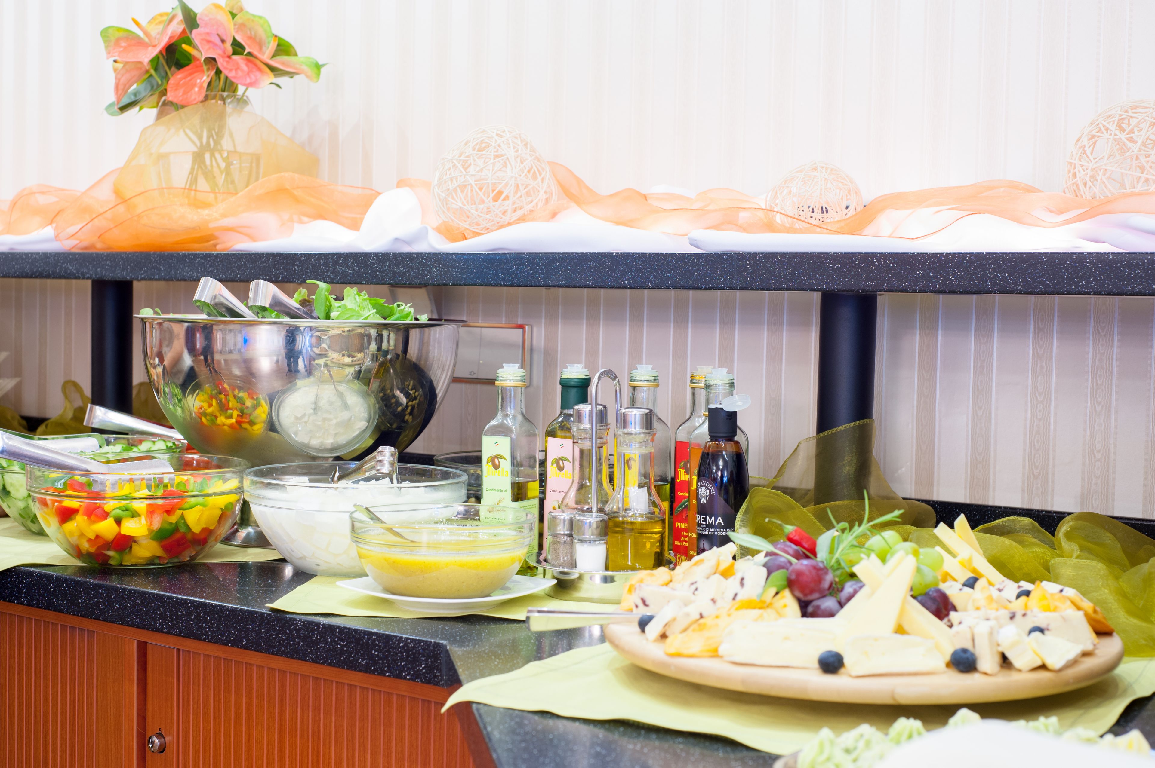 A buffet table with various food items, including a salad, cheese platter, and bowls of food, with decorative elements like a vase and a ball.
