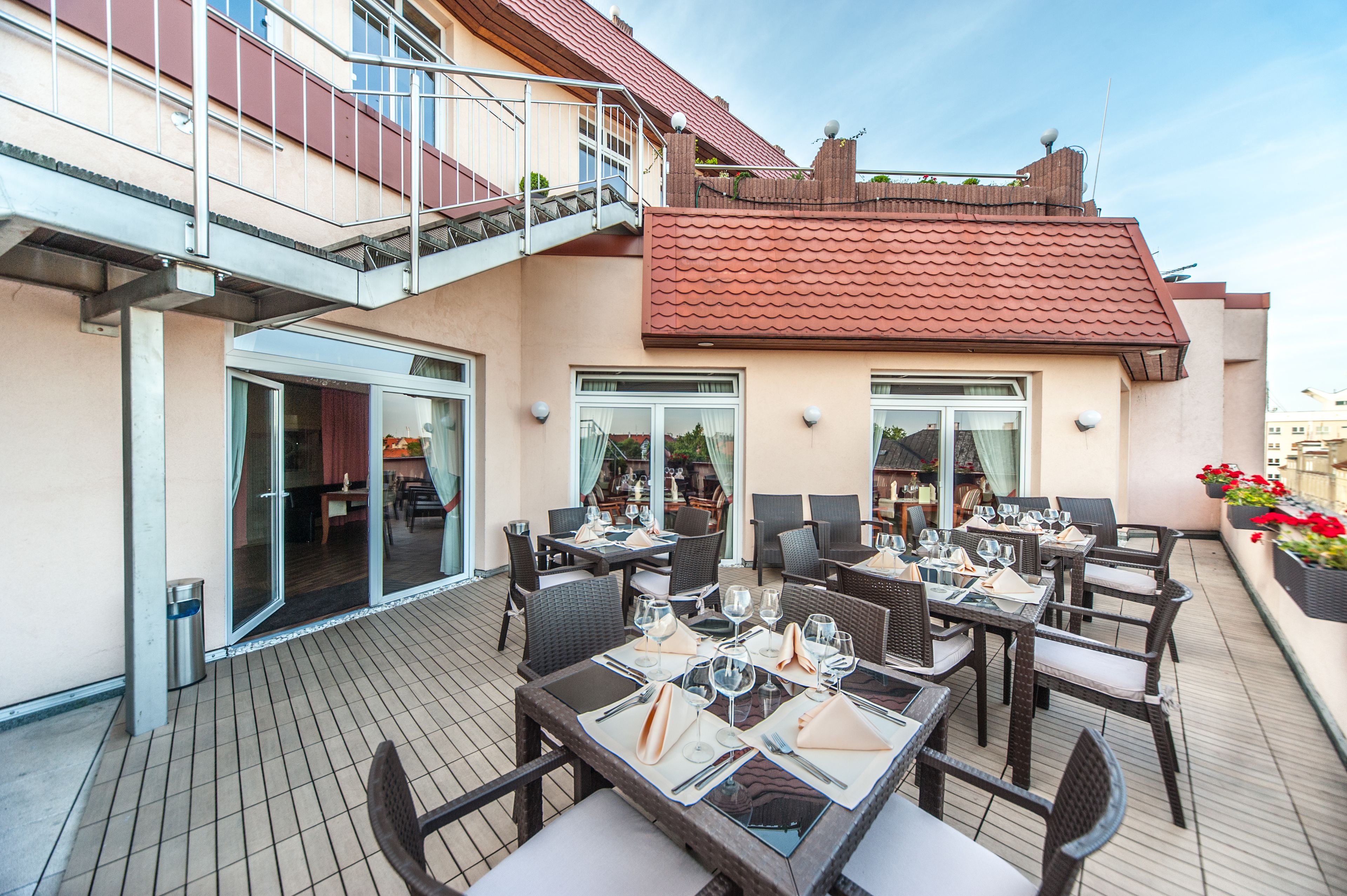 An outdoor dining area with tables and chairs, a staircase, and a building with a red roof.