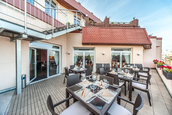 An outdoor dining area with tables and chairs, a staircase, and a building with a red roof.