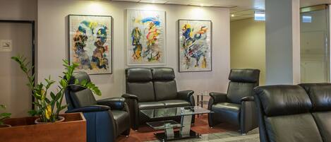 A lobby with leather chairs, a glass coffee table, and abstract art on the walls.