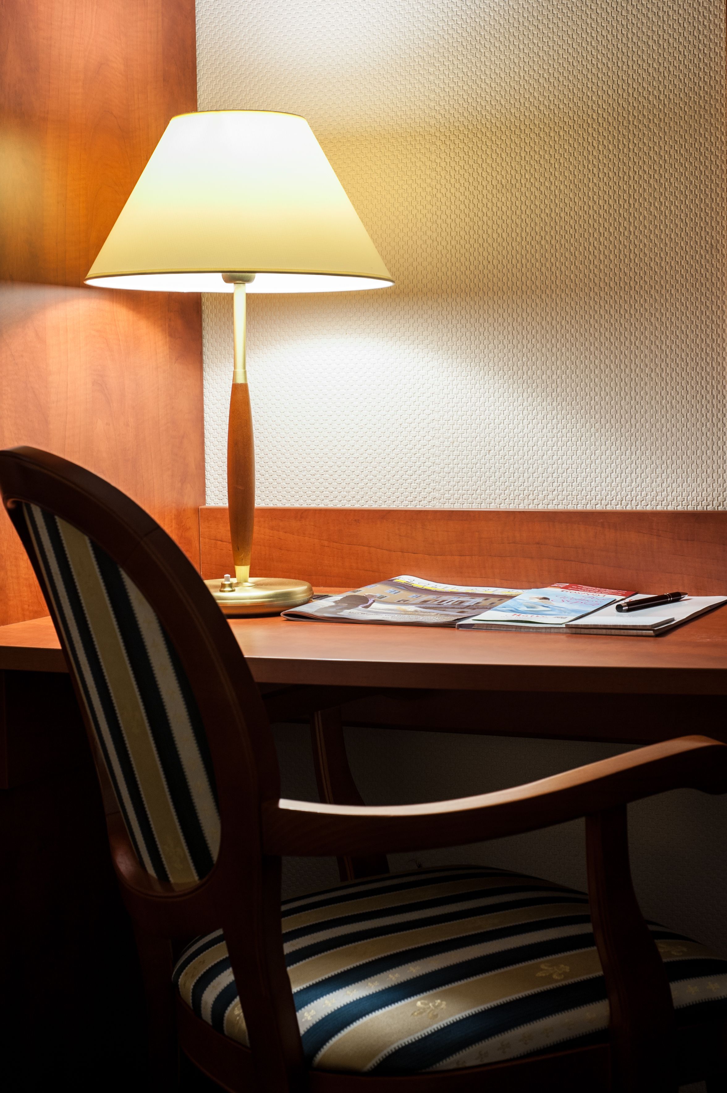 A wooden chair with a striped cushion, a table with a lamp, and a magazine.