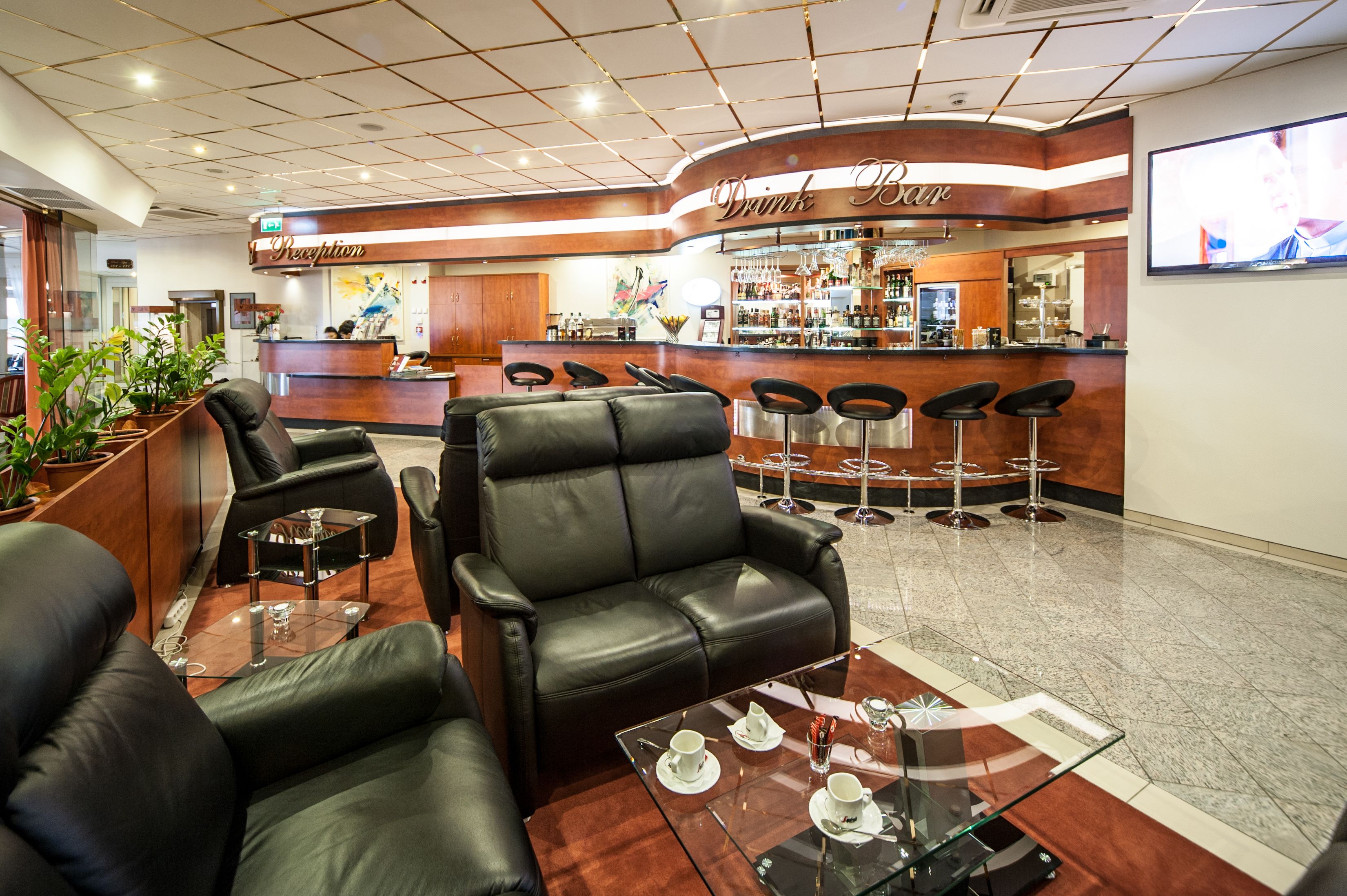 Un vestíbulo con asientos de cuero, una recepción, una zona de bar y una pantalla de televisión.