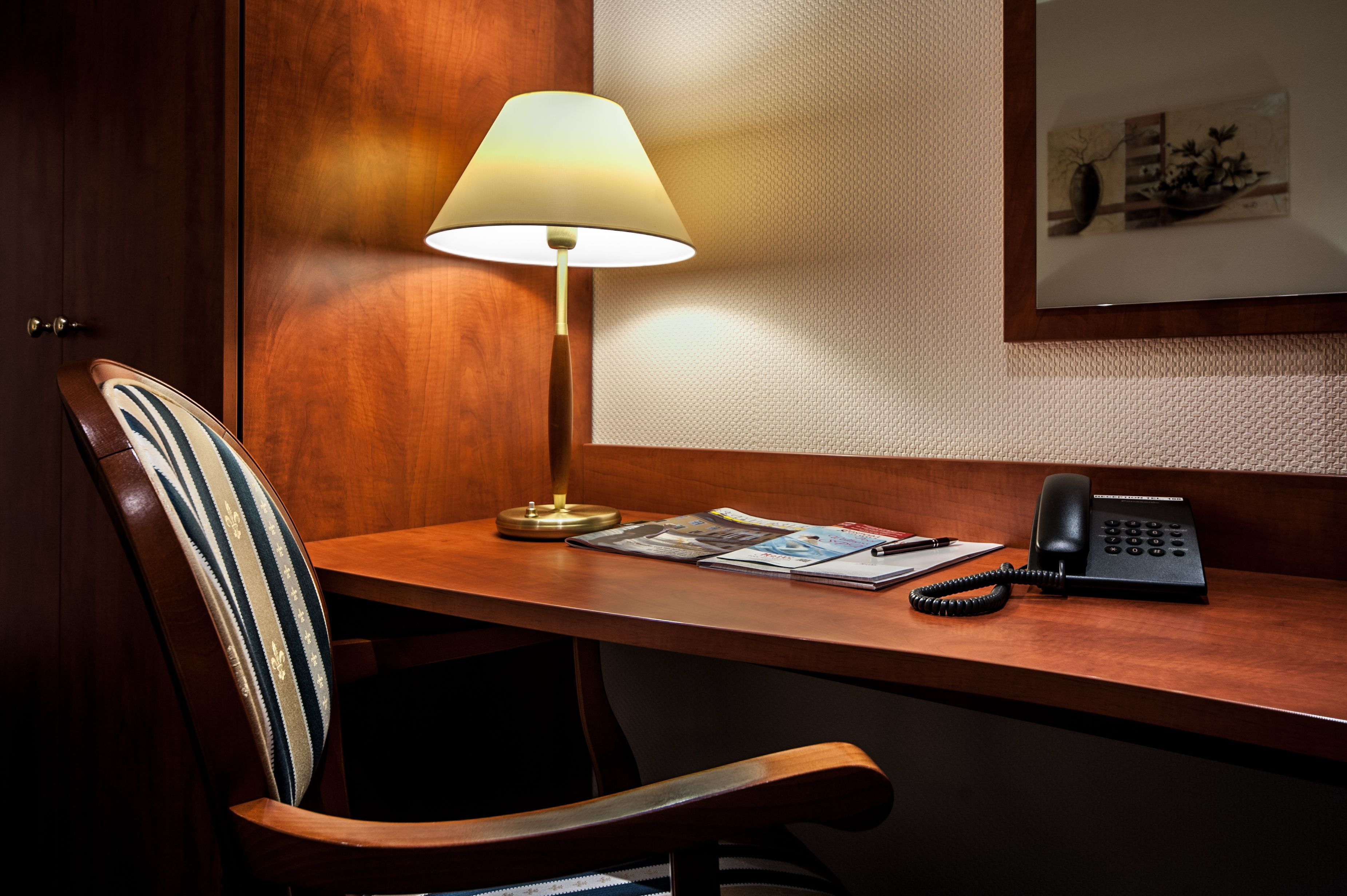 A wooden desk with a lamp, a telephone, and some magazines.