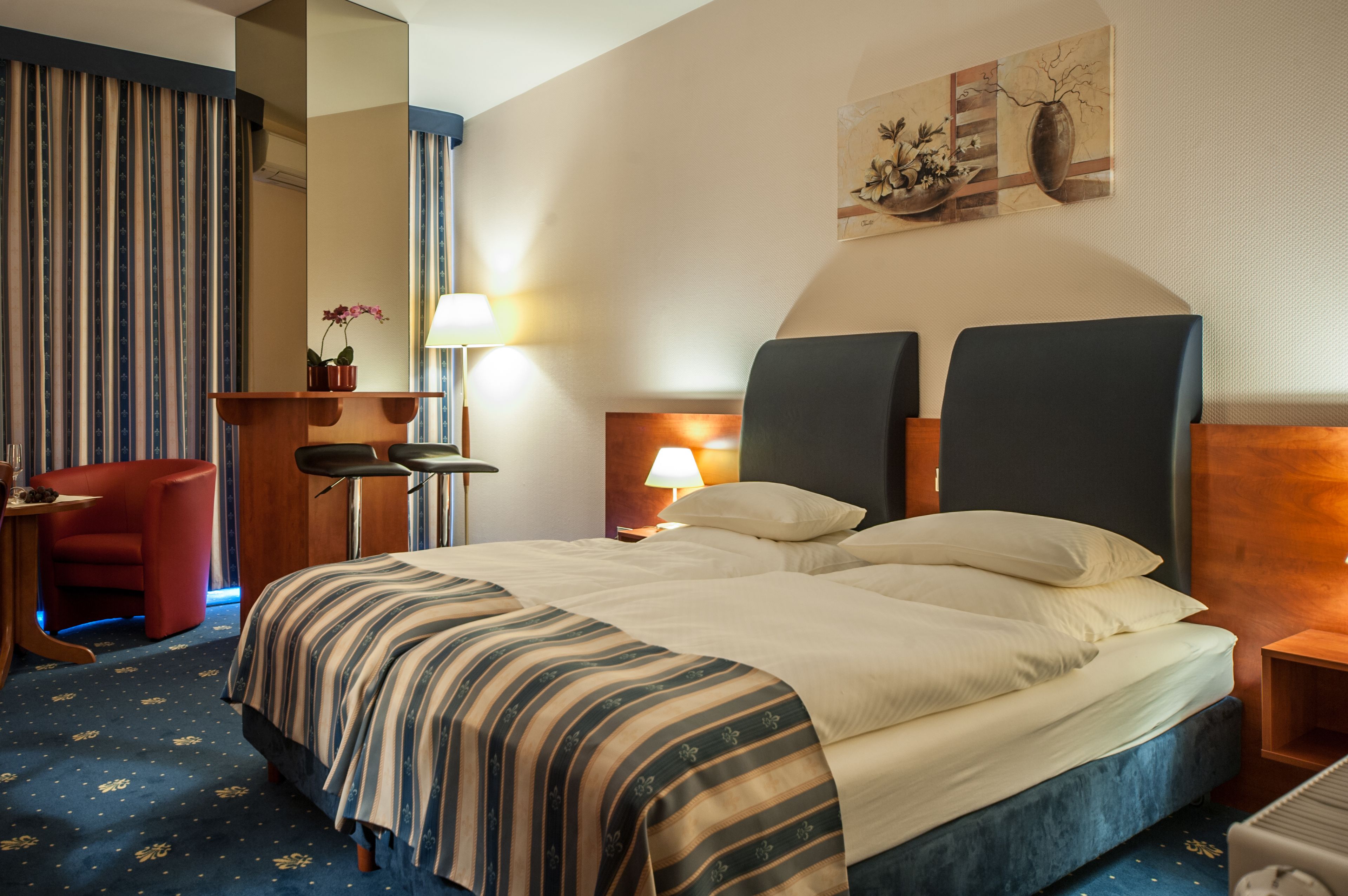 A hotel room with a large bed, a desk, a chair, and a lamp.