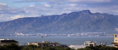 A coastal cityscape with mountains in the background, buildings in the foreground, and a view of the sea.