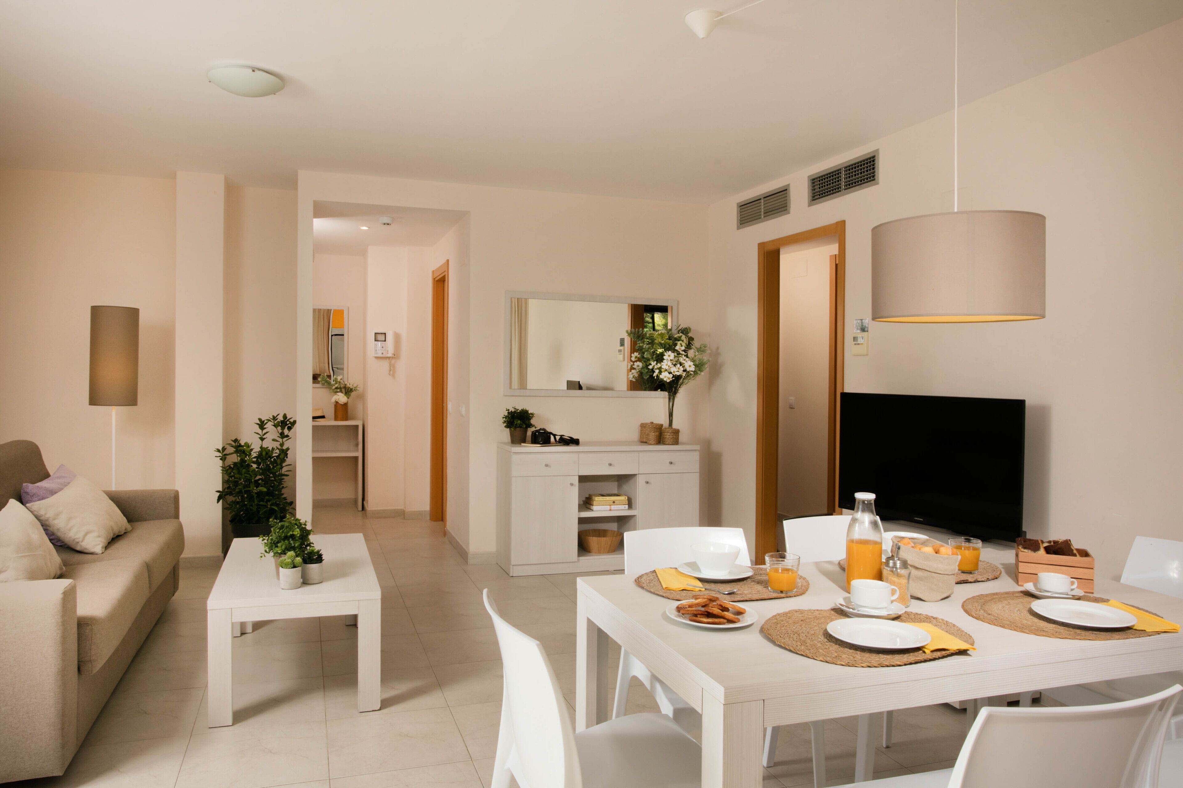 A modern living room with a sofa, coffee table, dining table set for breakfast, and a TV.
