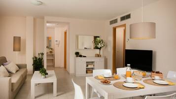 A modern living room with a sofa, coffee table, dining table set for breakfast, and a TV.