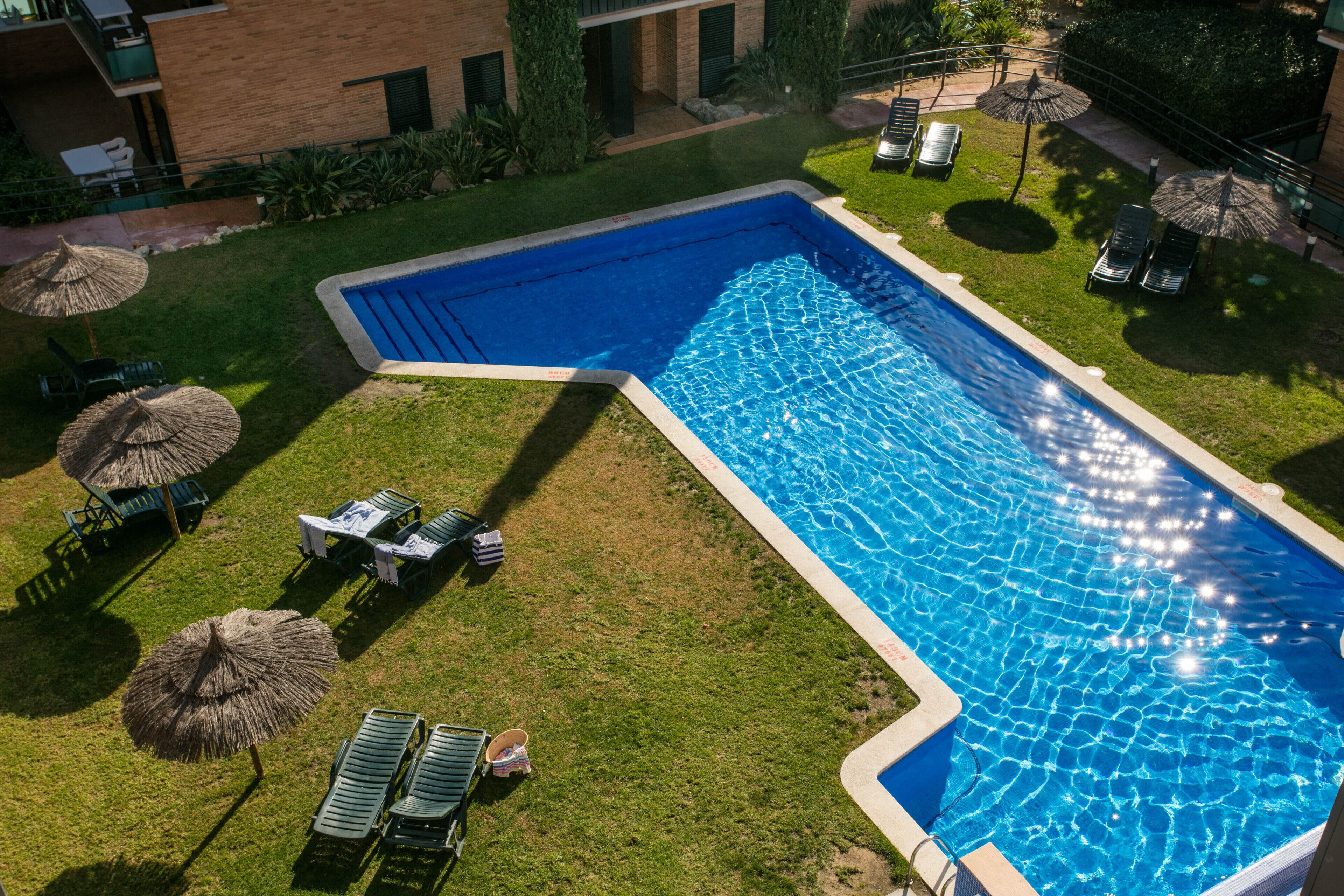 A rectangular swimming pool with a clear blue water surface, surrounded by a well-maintained lawn and several lounge chairs.