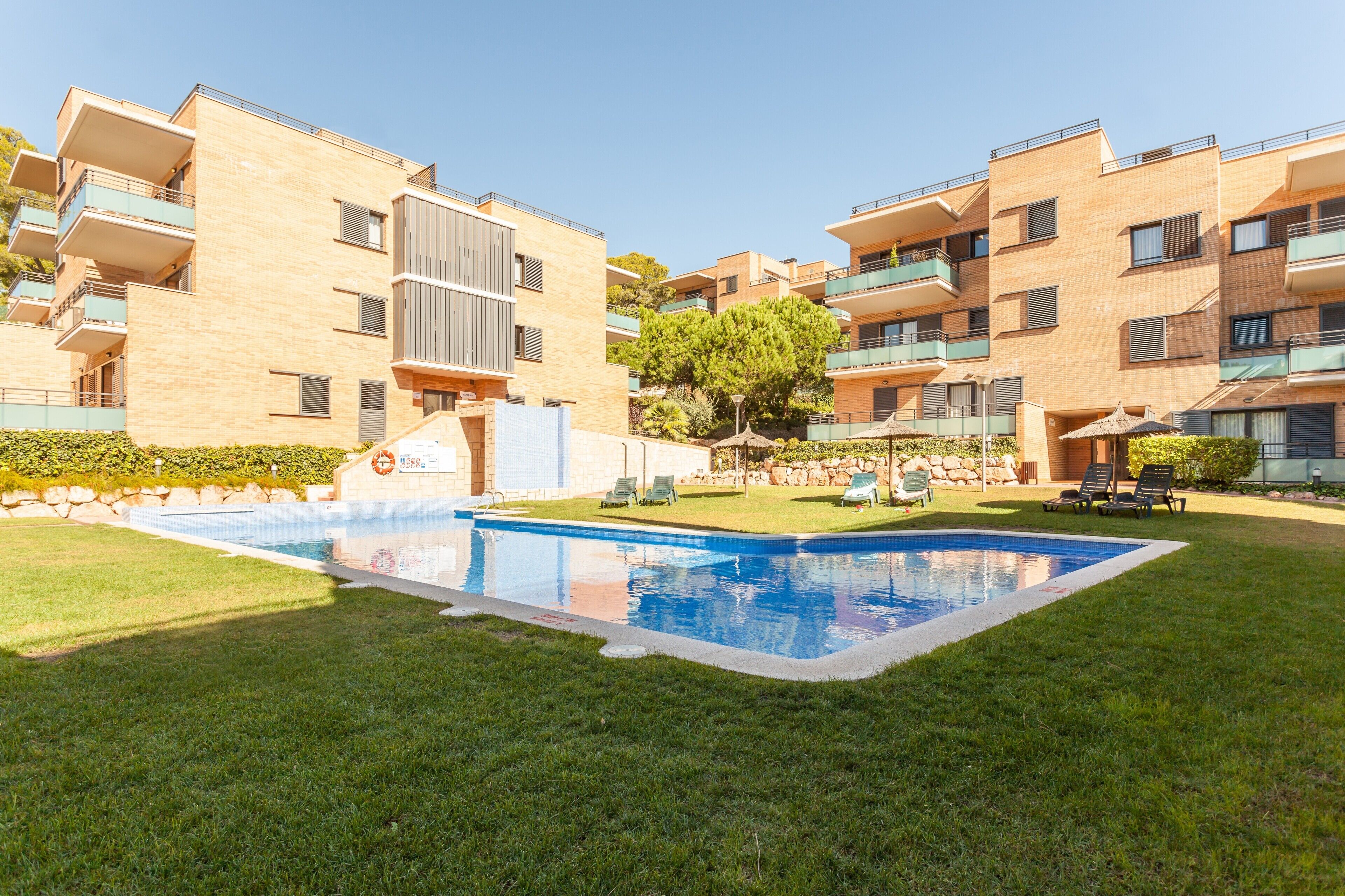 A modern apartment building with a swimming pool surrounded by grass and trees.