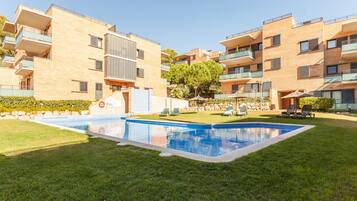 Un moderno edificio de apartamentos con piscina rodeada de césped y árboles.