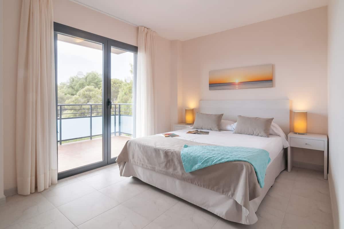 A bedroom with a large bed, a balcony view, and a painting on the wall.