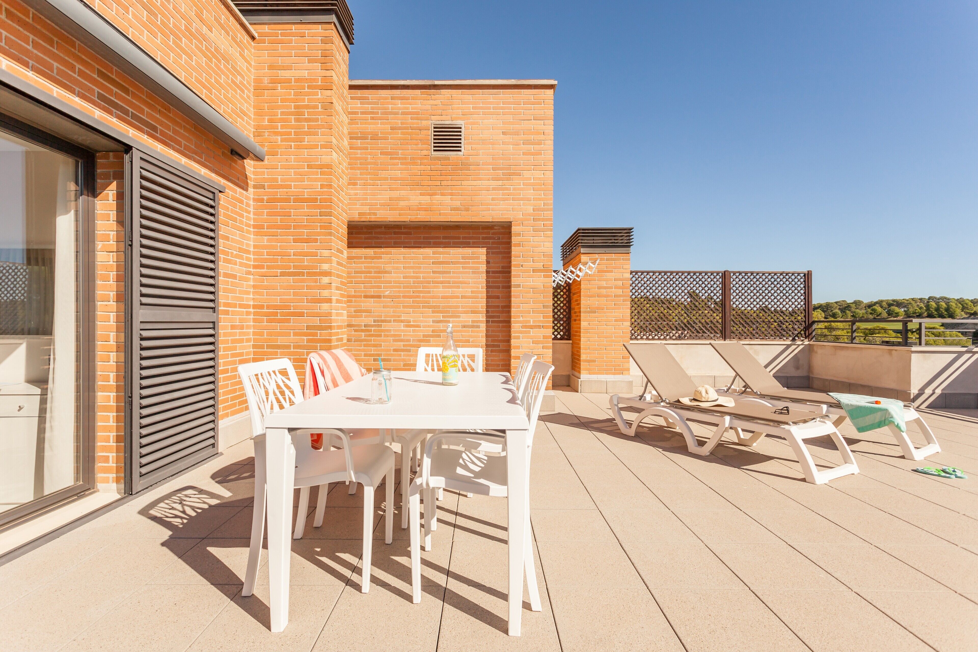 A rooftop terrace with a table and chairs, a sun lounger, and a view of the city.