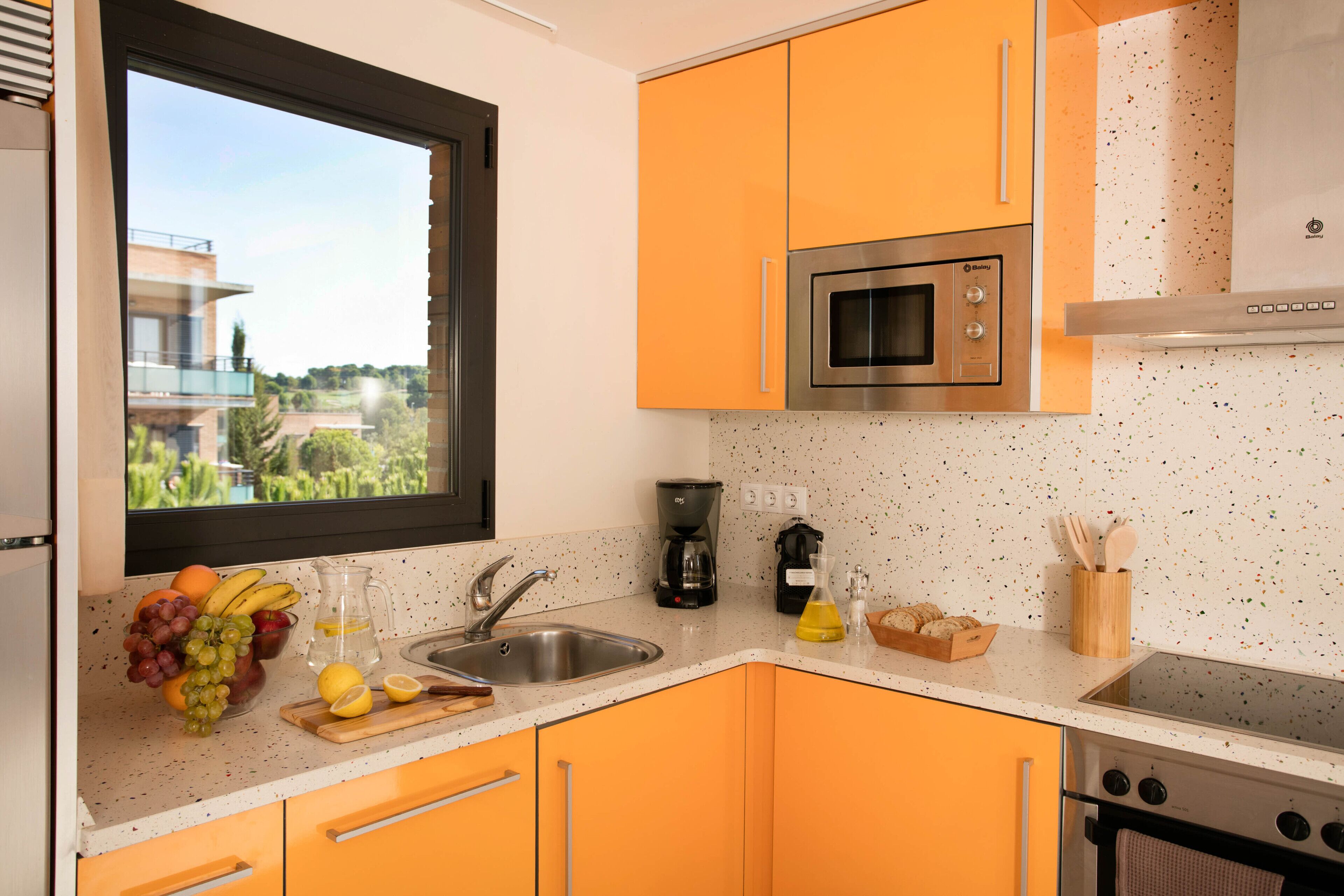 Een keuken met oranje kastjes, een roestvrijstalen spoelbak, een magnetron en een fornuis.