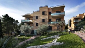 A multi-story residential building with balconies, a landscaped garden, and a clear sky.