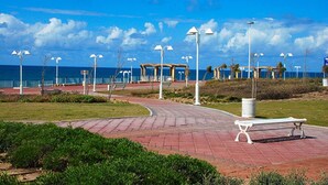 A paved walkway with benches, street lamps, and a view of the ocean. - Ga'aton Motel (Nahariya)