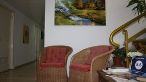 A hallway with wicker chairs, a painting of a house by a stream, and a sign for Ga'aton Motel. - Ga'aton Motel (Nahariya)