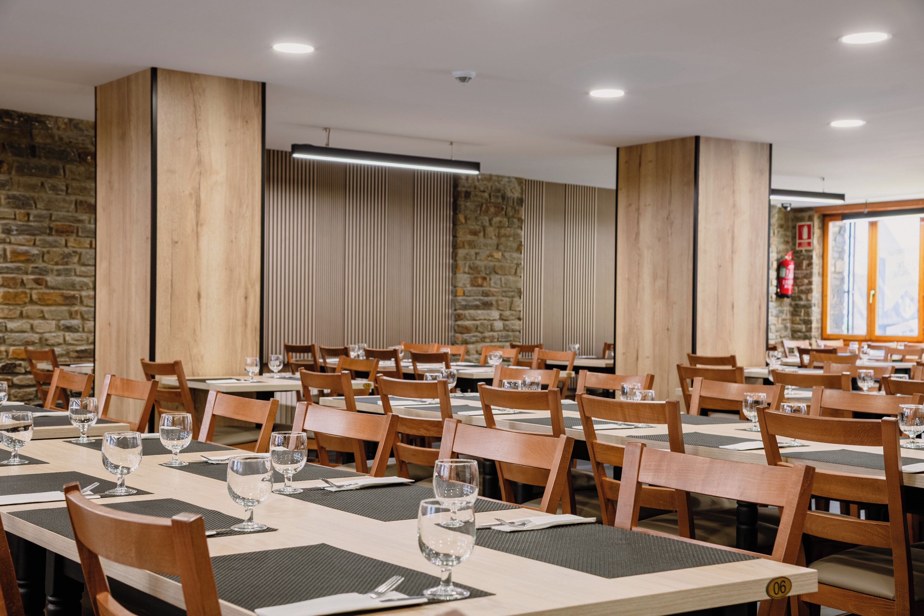 Un comedor con varias mesas y sillas, paredes de piedra y un extintor.