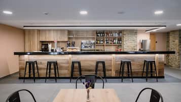 A modern bar area with a wooden counter, bar stools, a coffee machine, and a variety of bottles.