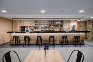A modern bar area with a wooden counter, bar stools, a coffee machine, and a variety of bottles. - Hotel Cal Ruiz (Pas de la Casa)