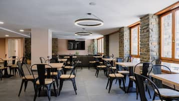 Um restaurante com várias mesas e cadeiras, paredes de pedra e uma televisão de tela plana na parede.