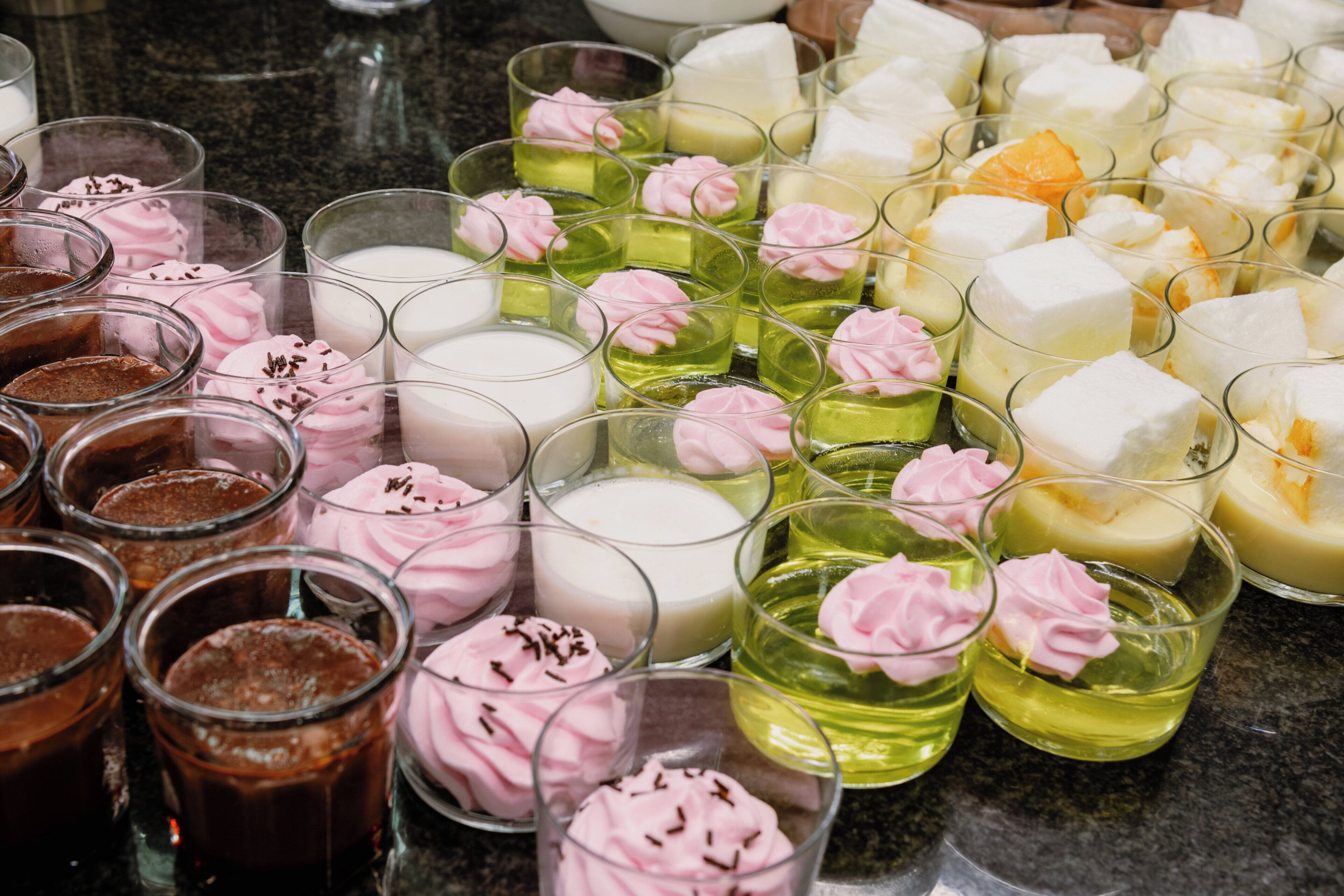 Variedad de postres en vasos transparentes, algunos con glaseado rosa y chispas.