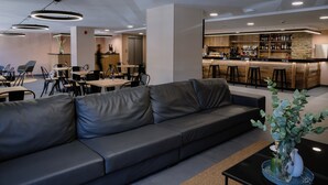 Un espacio lounge moderno con un sofá de cuero, mesas de comedor y una zona de bar con taburetes.