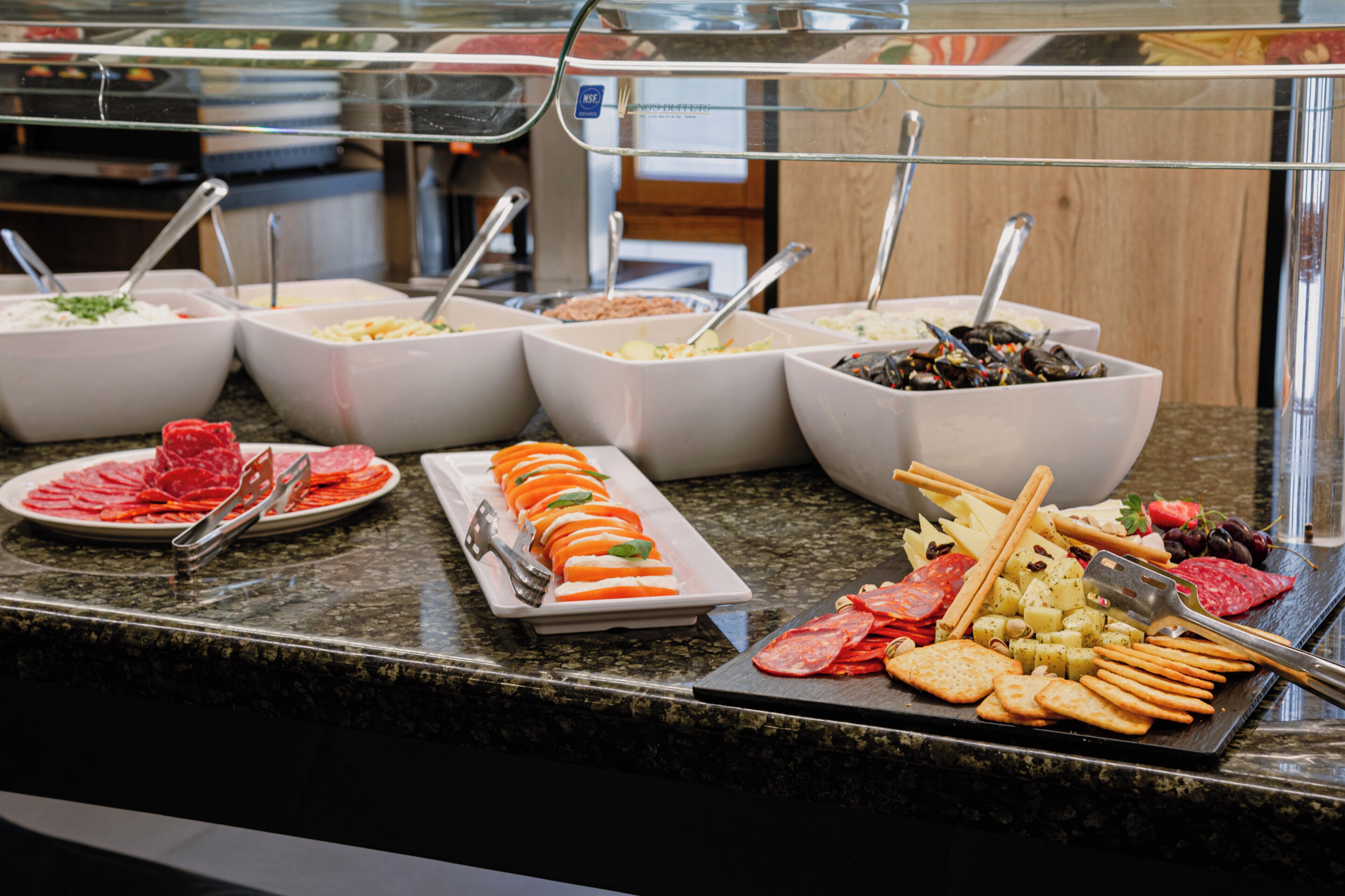 A buffet with various food items including sliced meats, cheeses, and fruits.
