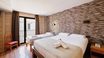 Een hotelkamer met twee bedden, een houten vloer, een balkon met gordijnen en een muur met baksteenmotief.