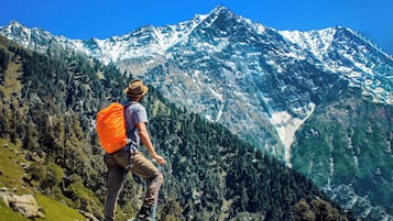 Un excursionista con una mochila naranja en la cresta de una montaña, con vistas a un valle con tiendas de campaña y picos nevados.