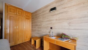 Una habitación con piso de madera, un armario de madera, una pequeña mesa de madera con una botella, vasos y un ramo de flores.