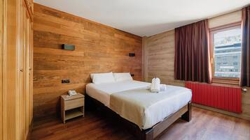 A hotel room with a wooden wall, a bed with white linens, a small bedside table with a phone, and a window with curtains.