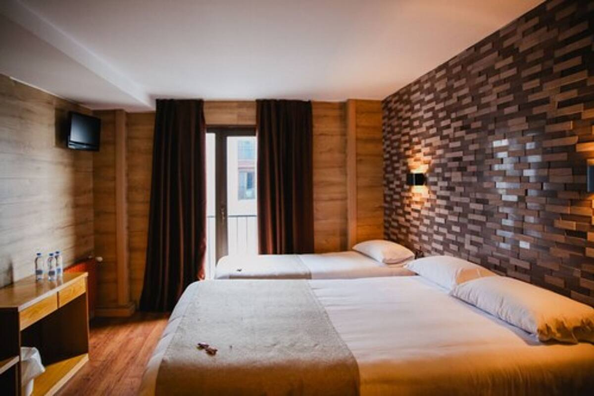 Une chambre d’hôtel avec deux lits, un mur en bois, une télévision et une fenêtre avec des rideaux.