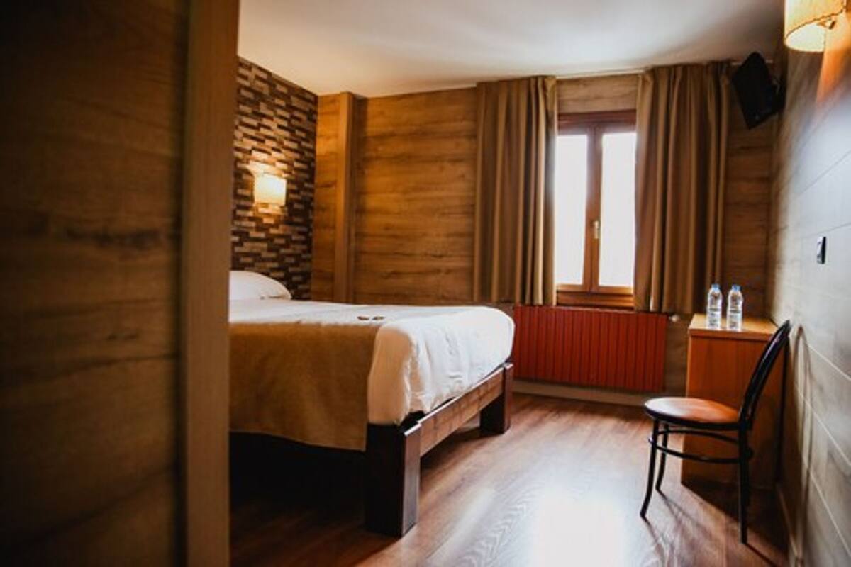 Une pièce aux murs lambrissés, comprenant un lit, une chaise, un radiateur et une fenêtre avec des rideaux.