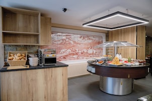 A buffet area with a coffee machine, a large mural, and a variety of food items.