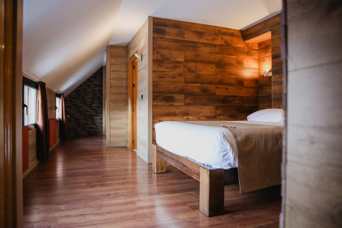 Une chambre à coucher avec une tête de lit en bois, un lit recouvert de linge de lit blanc et un plafond en pente.